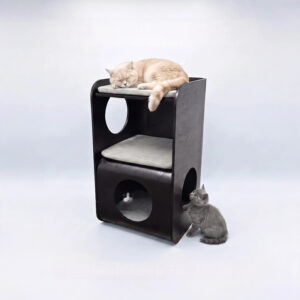 Black multi-level cat tower with oval and circular entry cutouts, three gray cushions, a cream cat sleeping on top, a black and white cat inside the cubby, and a grey kitten sitting beside it on a light grey background